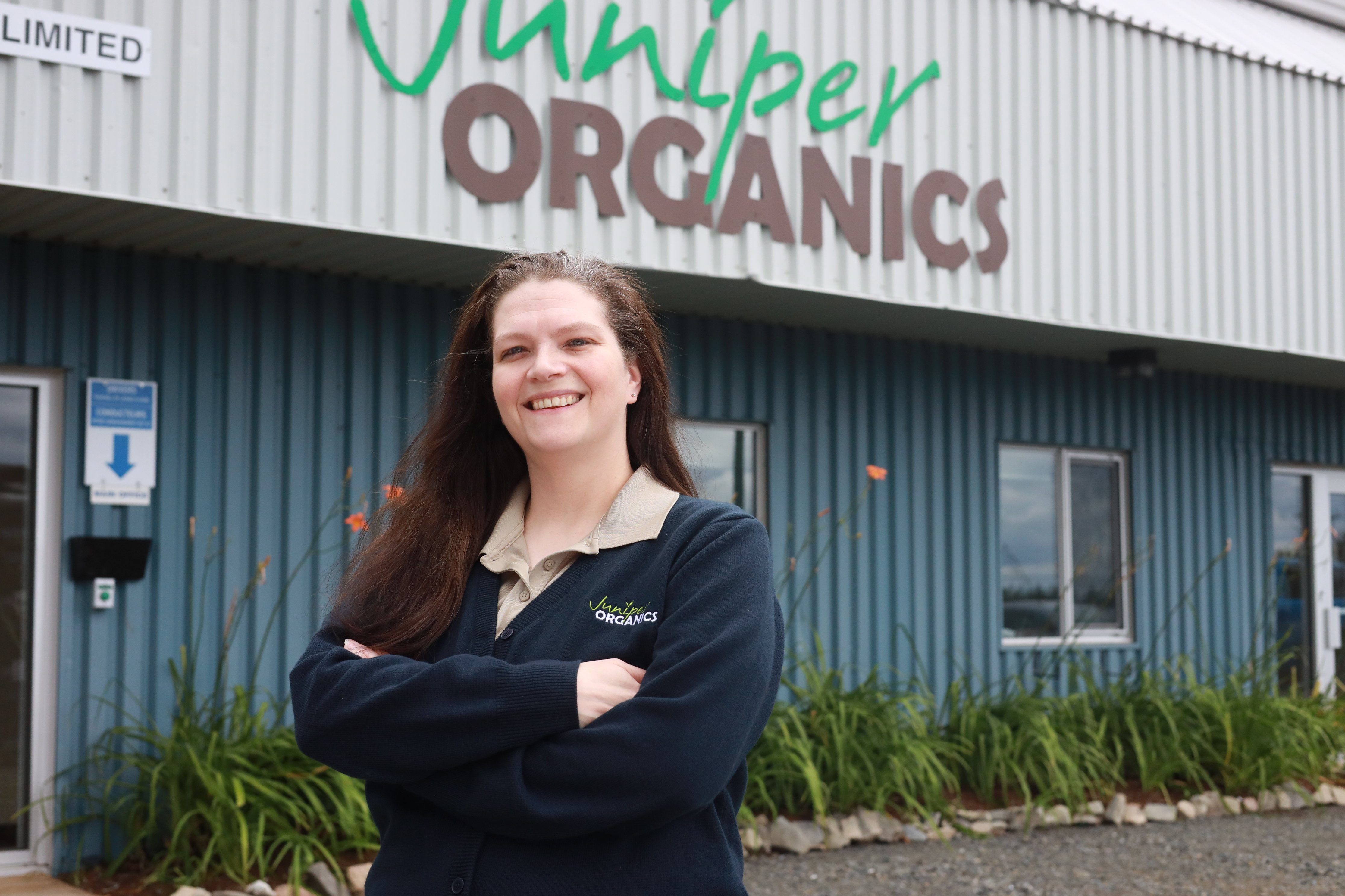 A smiling woman posing in front of a Juniper Organics storefront location